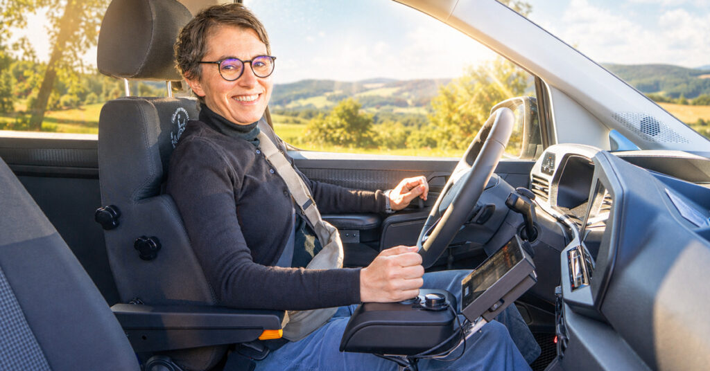 Hintergrund-Lead-Form-Space-Drive-Joystick-Gas-Bremsschieber-lächelnde-Kundin-Sonnenschein Autofahren mit Muskelerkrankung